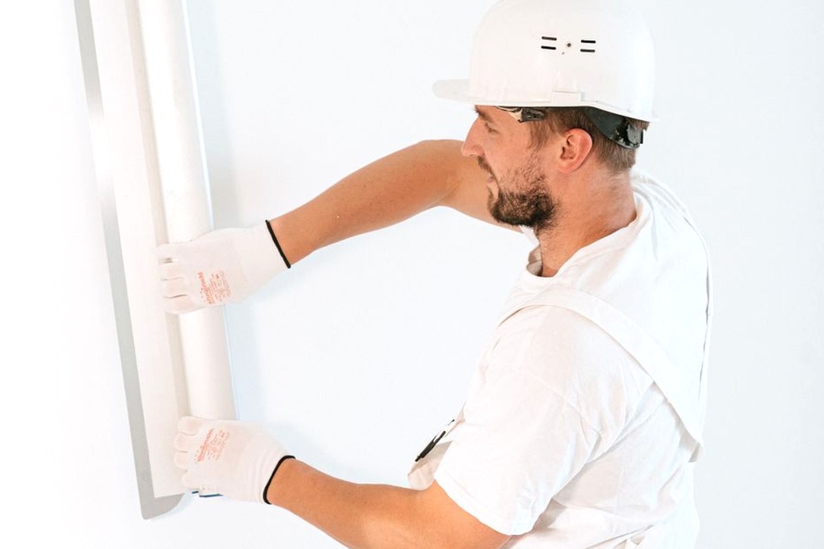 Professional construction worker installing drywall with gloves and helmet inside a building.